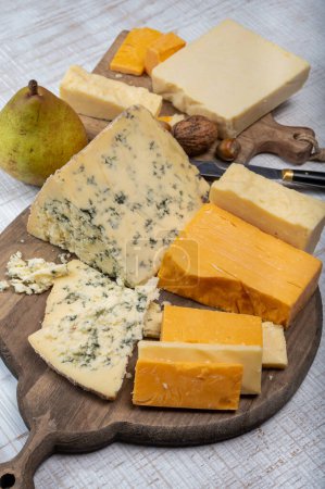 English cheeses collection, mature and coloured cheddar cheese and semi-soft, crumbly old stilton blue cheese close up on plate