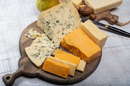 English cheeses collection, mature and coloured cheddar cheese and semi-soft, crumbly old stilton blue cheese close up on plate