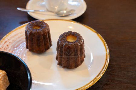 Canele, French pastry flavored with rum and vanilla, specialty of Bordeaux region, France, served on white plate with cup of black coffie in French restaurant