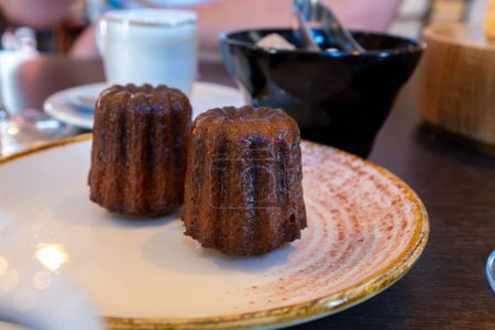 Canele, French pastry flavored with rum and vanilla, specialty of Bordeaux region, France, served on white plate with cup of black coffie in French restaurant