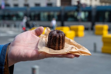 Canele, French pastry flavored with rum and vanilla, soft and tender custard center and  dark, caramelized crust specialty of Bordeaux region, France and streets of Bordeaux on background