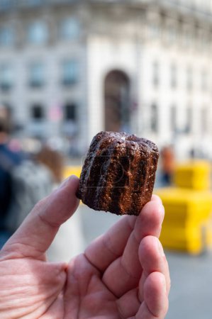 Canele, French pastry flavored with rum and vanilla, soft and tender custard center and  dark, caramelized crust specialty of Bordeaux region, France and streets of Bordeaux on background