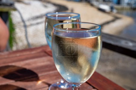 Drinking of white wine at farm cafe in oyster-farming village, with view on boats and water of Arcachon bay, Cap Ferret peninsula, Bordeaux, France in sunny day