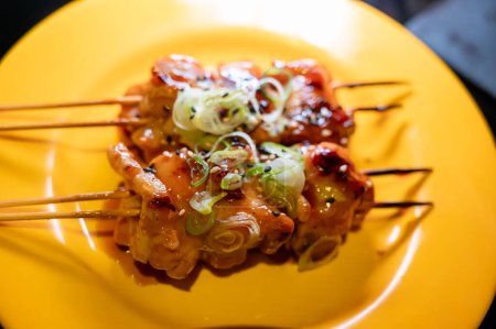 Wooden skewers with pieces of chicken fillet in teriyaki sauce from the grill served at yakitori restaurant in Milan, Italy, close up