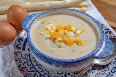 Bowl of homemade cream soup from white asparagus with chicken eggs, spring season, new harvest of Dutch, German white asparagus, cooking with asparagus vegetable