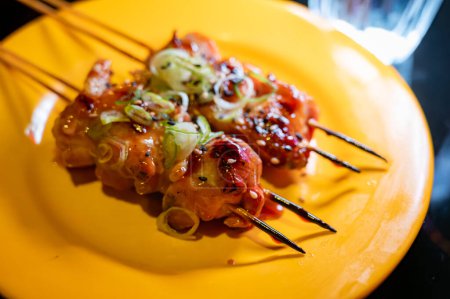 Brochetas de madera con trozos de filete de pollo en salsa teriyaki de la parrilla que se sirve en el restaurante yakitori en Milán, Italia, de cerca