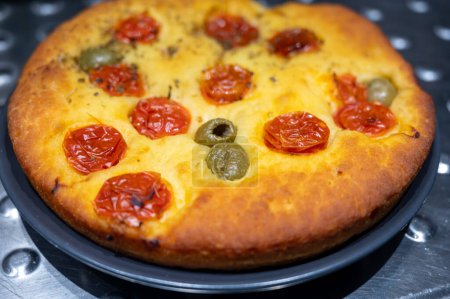 Tasty italian vegetarian food, fresh baked flat foccachia bread with small cherry tomatoes, olives and herbs close up