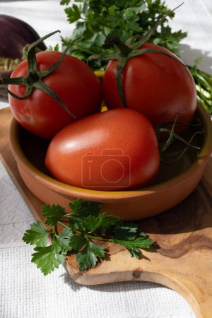 Ripe red Roma tomatoes in bowl with fresh herbs on table
