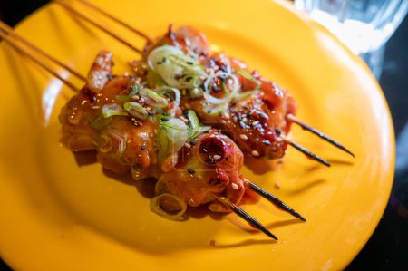 Wooden skewers with pieces of chicken fillet in teriyaki sauce from the grill served at yakitori restaurant in Milan, Italy, close up