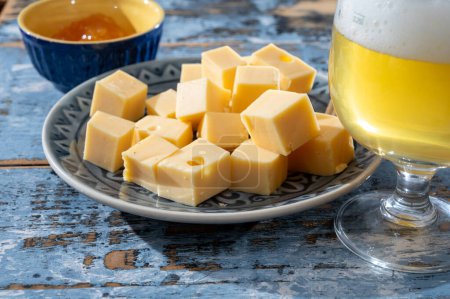 Colección de quesos, quesos duros maduros holandeses elaborados con leche de vaca en los Países Bajos en cubos y vaso de cerveza blanca