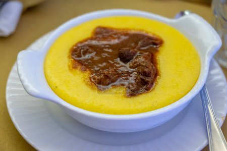 Traditional first course for lunch or dinner in Italy, yellow corn polenta porridge with stew served in Italian restaurant, Milan, Italy, close up