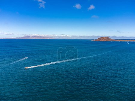 Aerial view Corralejo town, harbour, black rocks, blue water, Lobos and Lanzarote islands, Fuerteventura, Canary islands, Spain, winter sun vacation