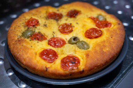 Tasty italian vegetarian food, fresh baked flat foccachia bread with small cherry tomatoes, olives and herbs close up