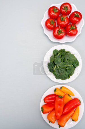 Fresh tomatoes, paprika, green spinach leaves, diet and health concept, weight loss, spinach on ceramic plate, copy space