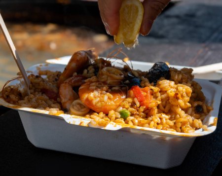 Street food in London, food court on Portobello road Saturday market, fresh prepared colorful paella with rice and sea food in box with lemon, ready to eat