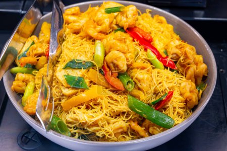 Comida asiática local, plato de fideos singapurenses con verduras, camarones fritos y carne de pollo en un tazón