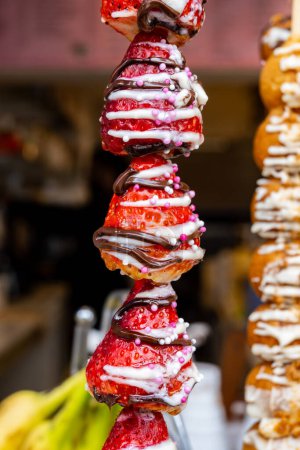 Candy shop in London, various sweet profiteroles and fresh strawberries with chocolate decoration on skewers ready to eat