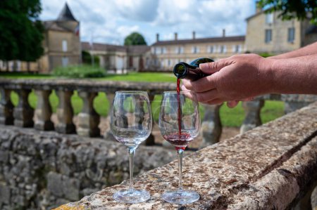 Gläser französischen trockenen Rotweins in alter Weindomäne auf den Weinbergen von Graves im Dorf Portets und im Hintergrund ein altes Winzerschloss, Bordeaux, Frankreich