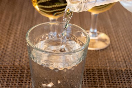 Kellner gießt Mineralwasser aus der Glasflasche in ein Glas, Verpflegungskonzept, Nahaufnahme