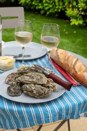 Plate with fresh live raw oysters seashells with citron, bread, butter and white wine served at restaurant in oyster-farming village, Arcachon bay, Gujan-Mestras port, France