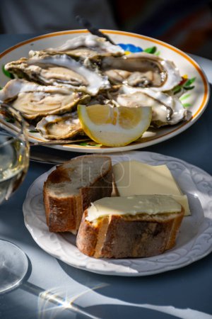 Plate with fresh live raw oysters seashells with citron, bread, butter and white wine served at restaurant in oyster-farming village, Arcachon bay, Gujan-Mestras port, France