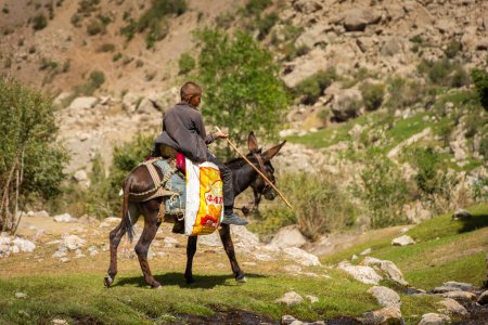 Foto de Haft Kul, Tayikistán, 21 de agosto de 2023: Pequeño niño montando un burro en las montañas Fann - Imagen libre de derechos