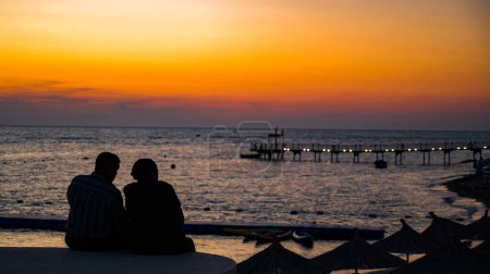 Téléchargez les photos : Couple amoureux regardant coucher de soleil ensemble. silhouette de derrière assis profiter de la vue coucher de soleil mer en vacances. - en image libre de droit