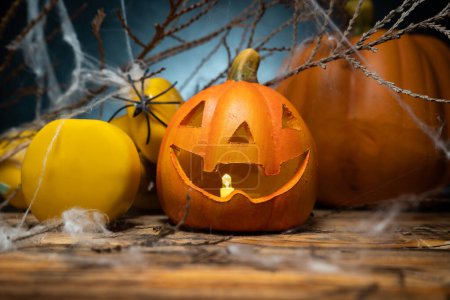 Photo for Yellow gym dumbbells, small ceramic Halloween Jack O Lantern figurine and autumn pumpkin in background, covered with spider web. Healthy fitness lifestyle fall composition. - Royalty Free Image
