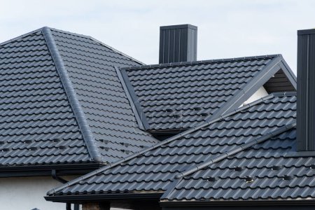 Neues schwarzes Metalldach eines Hauses mit Schornstein. Bedachung von Metallprofilen. Dachkonstruktion aus Metall.