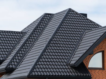 Das Haus, dessen Dach mit schwarzen Metallziegeln gedeckt ist. Schwarze Ziegeldächer auf einem neuen Haus.