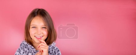 Portrait or advertising banner with space to insert text and a beautiful smiling little brunette girl 8 years old on a pink background in pajamas close-up. High quality photo
