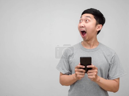 Téléchargez les photos : Jeune homme asiatique chemise grise tenir téléphone portable se sent choqué en regardant l'espace de copie isolé - en image libre de droit