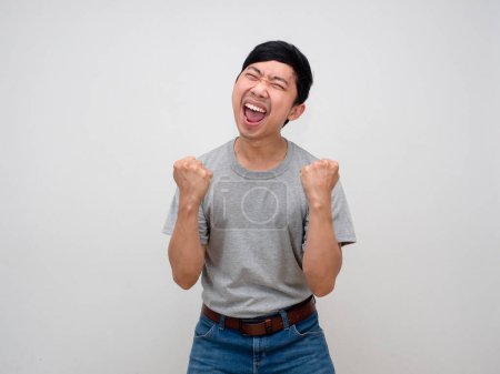 Téléchargez les photos : Positif asiatique homme chemise grise montrer poing vers le haut se sent heureux avec succès, Homme satisfait heureux de la victoire isolé - en image libre de droit