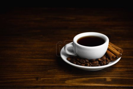 A cup of aromatic black coffee. Morning espresso or Americano coffee for breakfast in a beautiful cup. Cinnamon sticks. Wooden background.