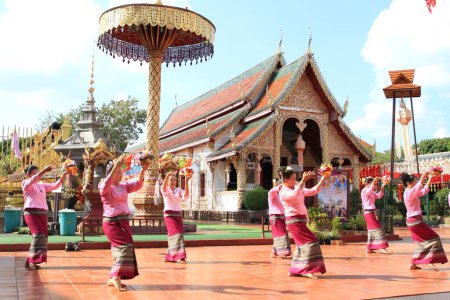 Foto de LAMPHUN -THAILAND: November 11, 2023:  Beautiful senior women perform an ancient Thai dance showing dancing in buddhist religious ceremony in TWat Phra That Haripunchai Woramahawihan. Thai nail dance with flower. - Imagen libre de derechos
