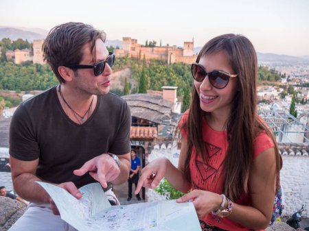 Ein paar gut aussehende Touristen vor der Alhambra mit Sonnenbrille und Landkarte, lachend, während er auf die Landkarte zeigt