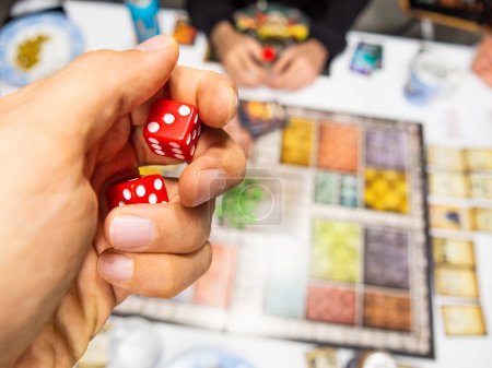 Hand mit roten sechsseitigen Würfeln auf dem Spielbrett von oben mit anderen echten Spielern