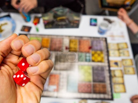 Hand mit roten sechsseitigen Würfeln, die eine Eins und eine Drei auf dem Spielbrett von oben mit anderen realen Spielern zeigen