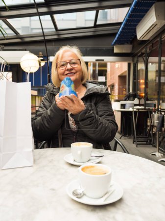 Lächelnde blonde Seniorin zeigt handgemachtes Krug-Geschenk zum Muttertag im Café