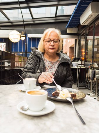 Senior-Blondine mit Brille teilt süßes Brownie-Dessert besorgt in Café
