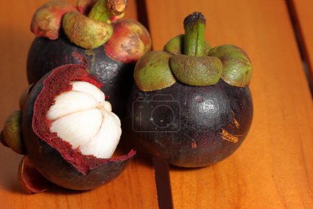 Téléchargez les photos : Ensemble de fruits mûrs de mangoustan avec un noyau délicieux. Le fruit est violet foncé ou rouge. connu sous le nom de mangoustan pourpre. Mangoustan sur fond en bois. Fruits de prévention du cancer. Garcinia mangostana - en image libre de droit
