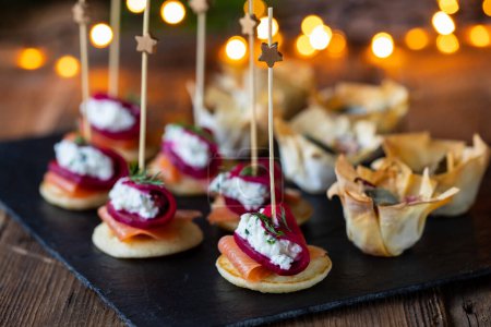Foto de Canapés de Navidad con blinis con salmón, remolacha y queso de cabra y tazas de pastelería de filo - Imagen libre de derechos