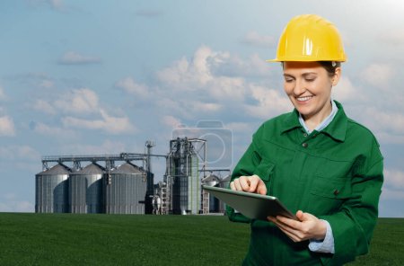 Mujer ingeniera con tableta digital sobre fondo de silos agrícolas para la producción de biocombustibles 