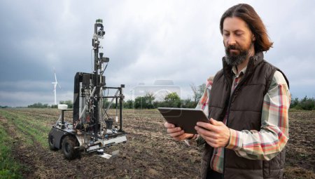 Landwirt steuert autonomen Roboter zur Messung der Bodenqualität in einem landwirtschaftlichen Feld. Smart-Farming-Konzept. 