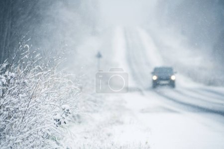 The car is driving on a winter road in a blizzard. Focus on foreground.