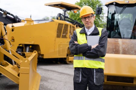 Engineer with digital tablet next to road construction machine.