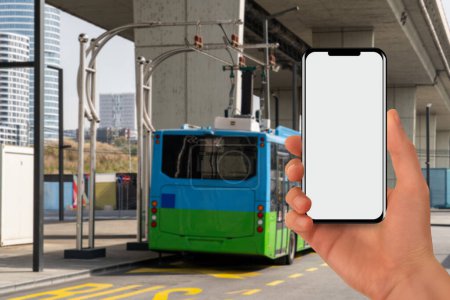 Eine Hand mit einem Telefon auf dem Hintergrund eines aufladenden Elektrobusses.