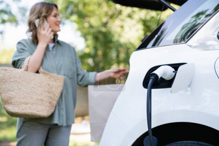 Woman with shopping bag next to a charging electric car..