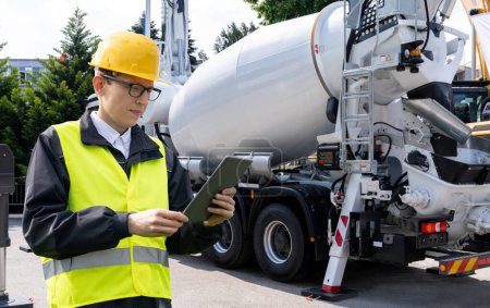Worker with digital tablet next to truck-mounted concrete pump with mixer