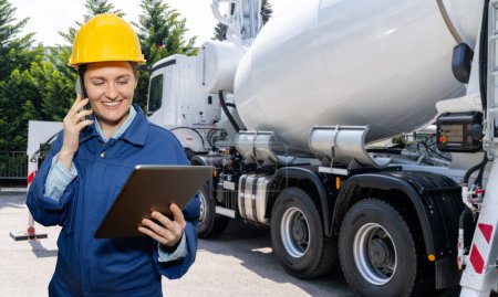 Female worker with digital tablet next to truck-mounted concrete pump with mixer.